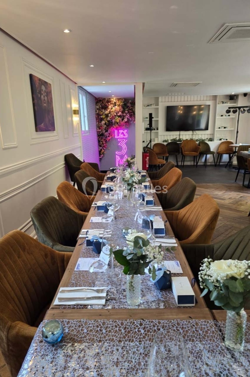 Table dressée pour un événement dans une salle élégante avec chaises en velours, décor floral et néon lumineux en arrière…