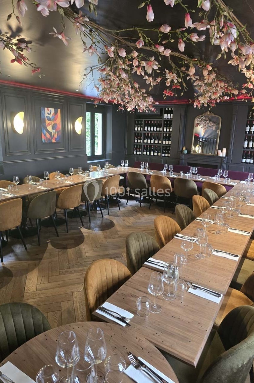 Salle de restaurant élégante avec tables en bois, chaises rembourrées et décoration florale suspendue au plafond.
