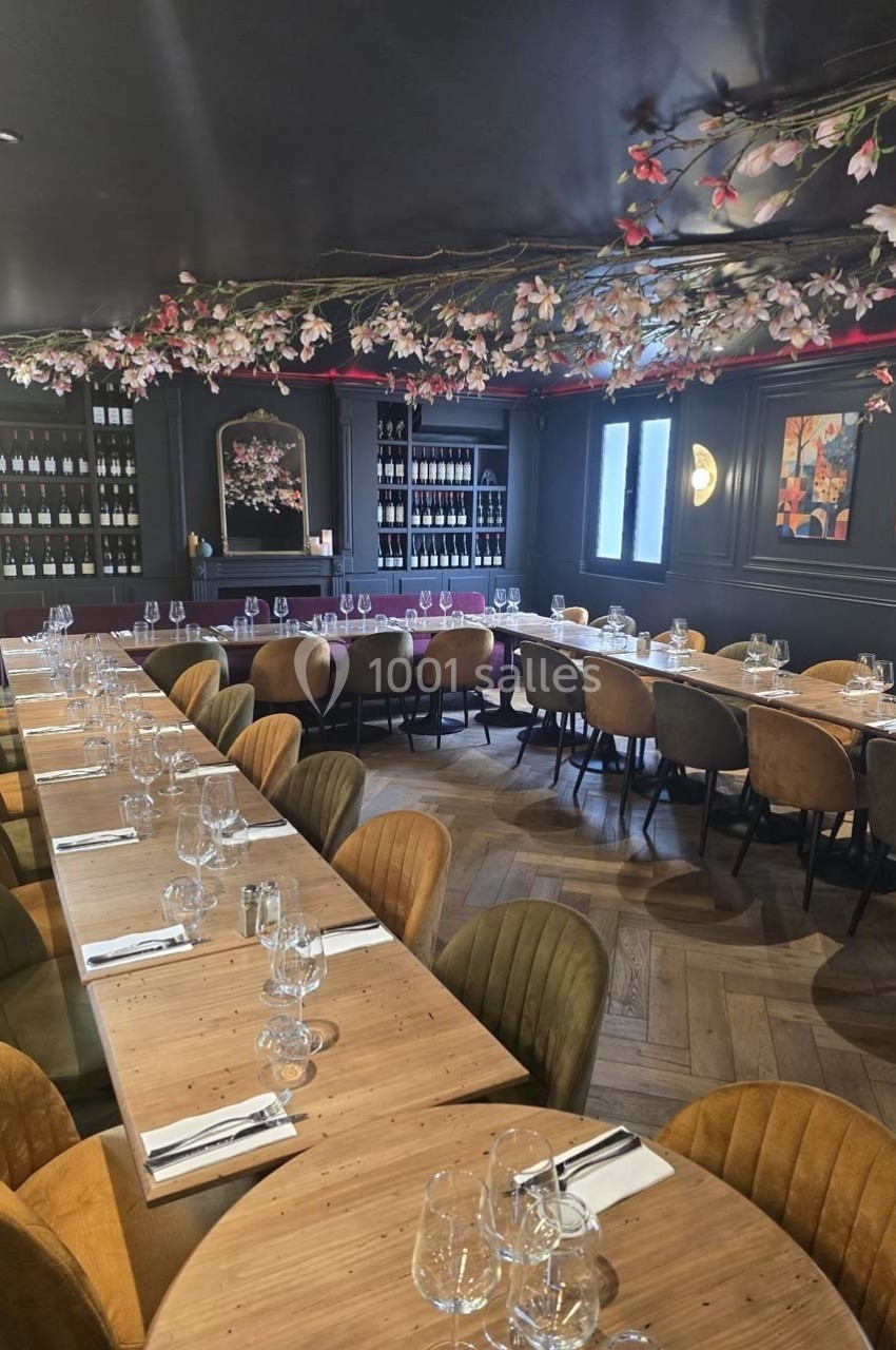 Salle de restaurant élégante avec longues tables en bois, chaises colorées et décor floral suspendu au plafond.