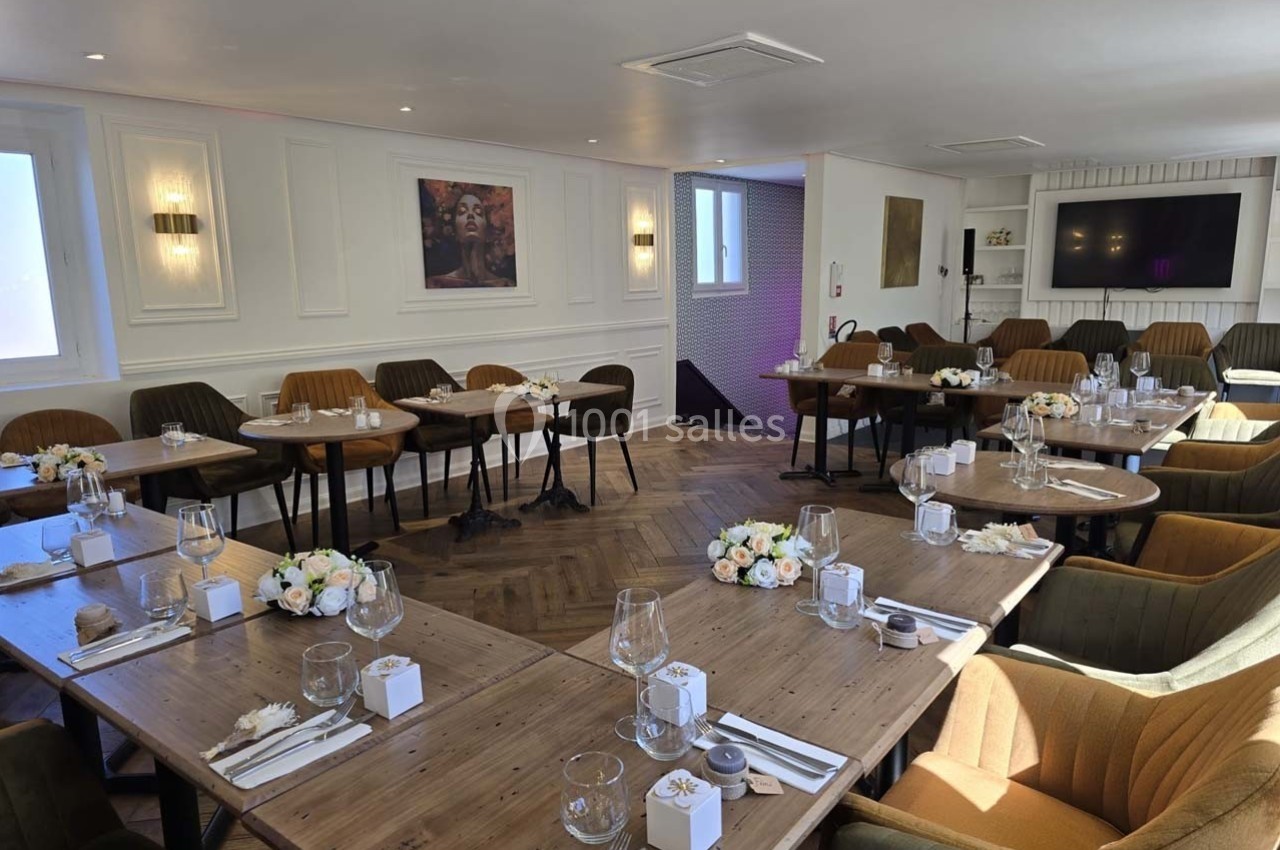 Salle lumineuse aménagée avec des tables en bois disposées en U, décorée de bouquets de fleurs et de vaisselle élégante.