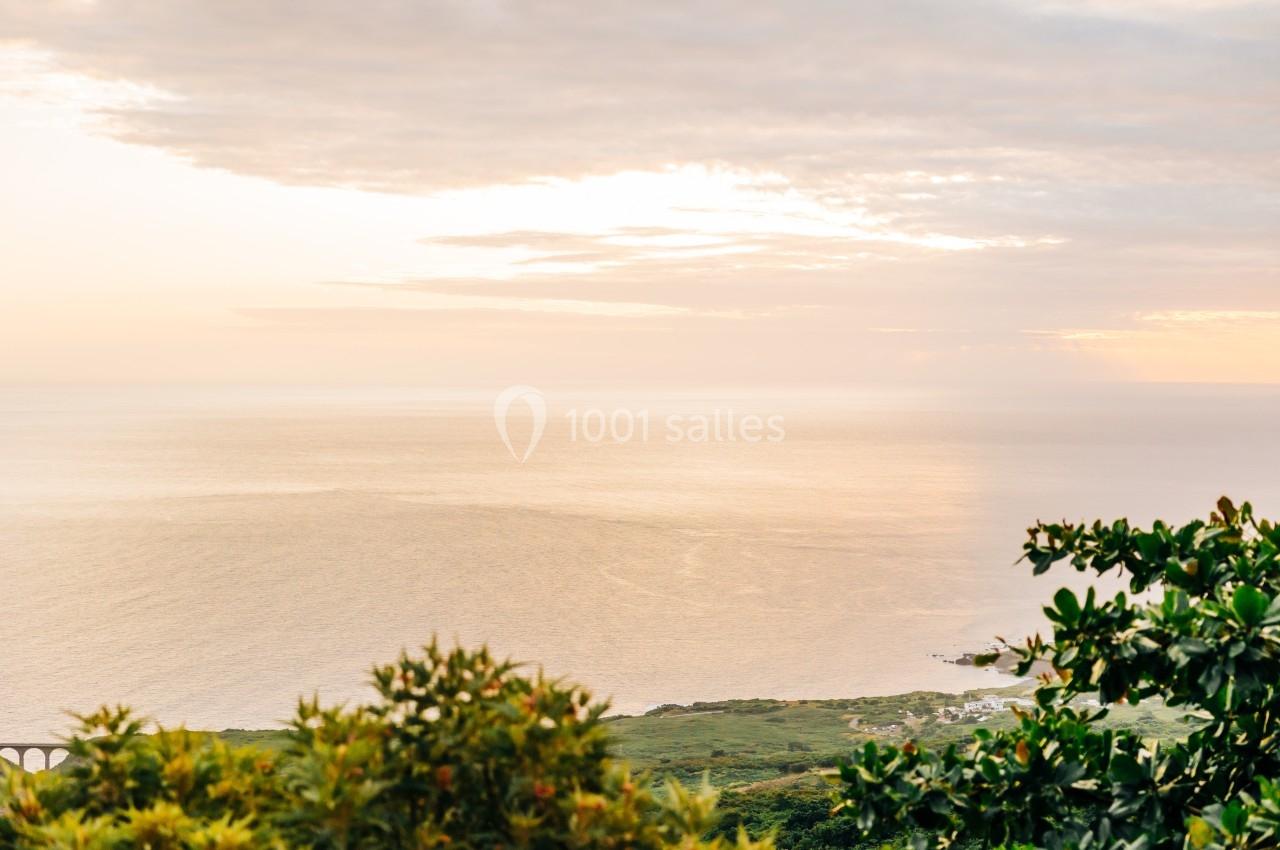 Vue sur une étendue d'océan au coucher du soleil, entourée de végétation verdoyante au premier plan.