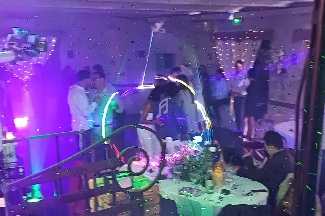 Des invités dansent et discutent dans une salle de réception décorée avec des lumières colorées et des effets lumineux.