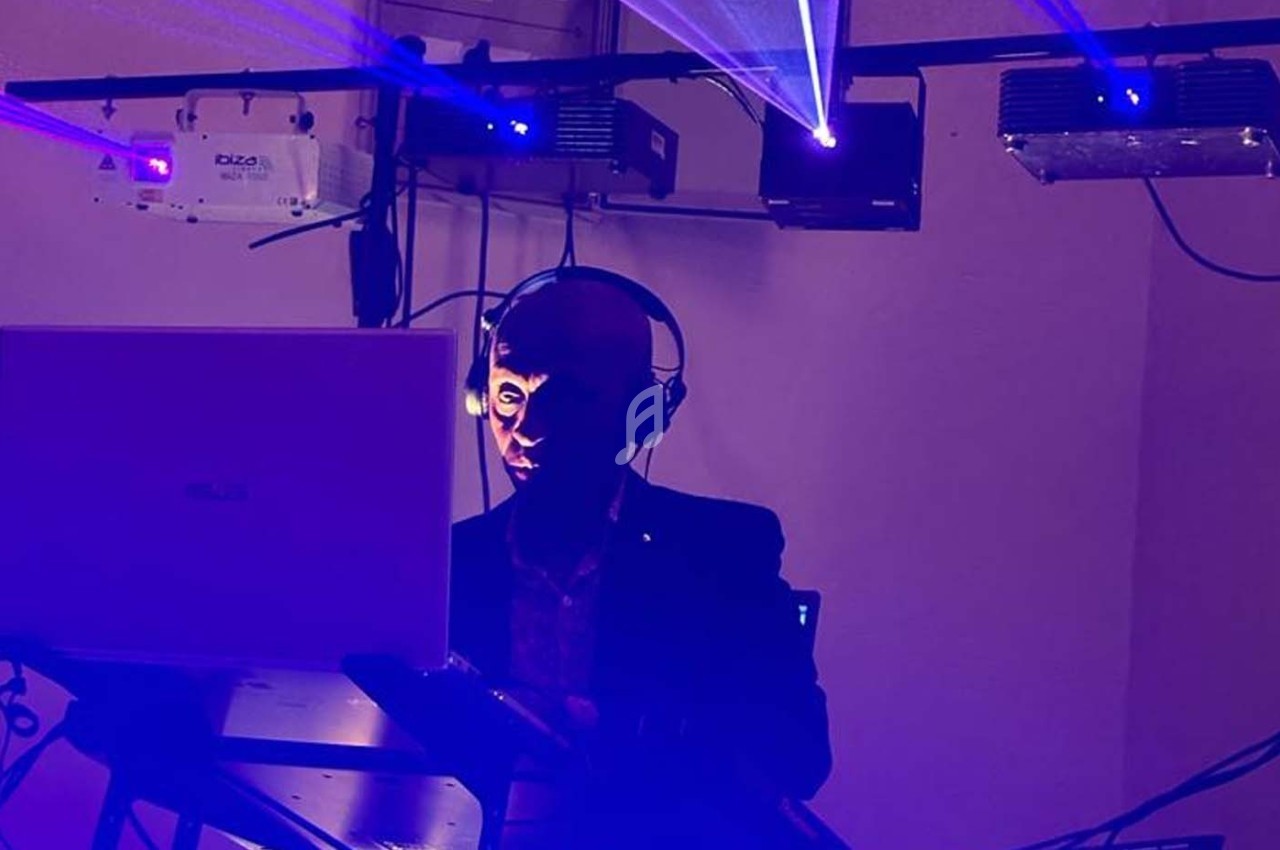 Un DJ mixe sur son équipement dans une ambiance lumineuse avec des faisceaux laser violets.
