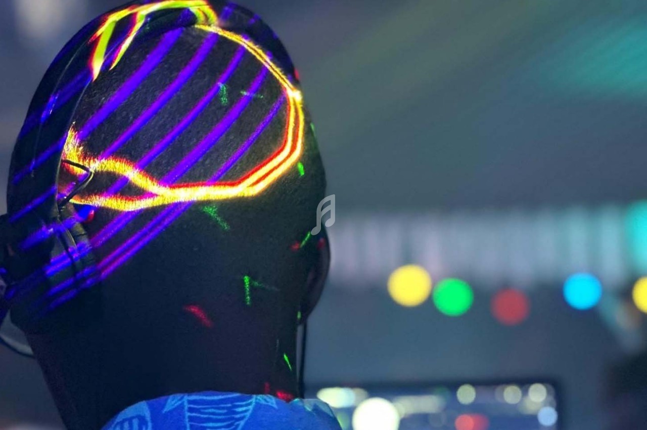 Un DJ de dos portant un casque, éclairé par des lumières colorées dans une ambiance festive.