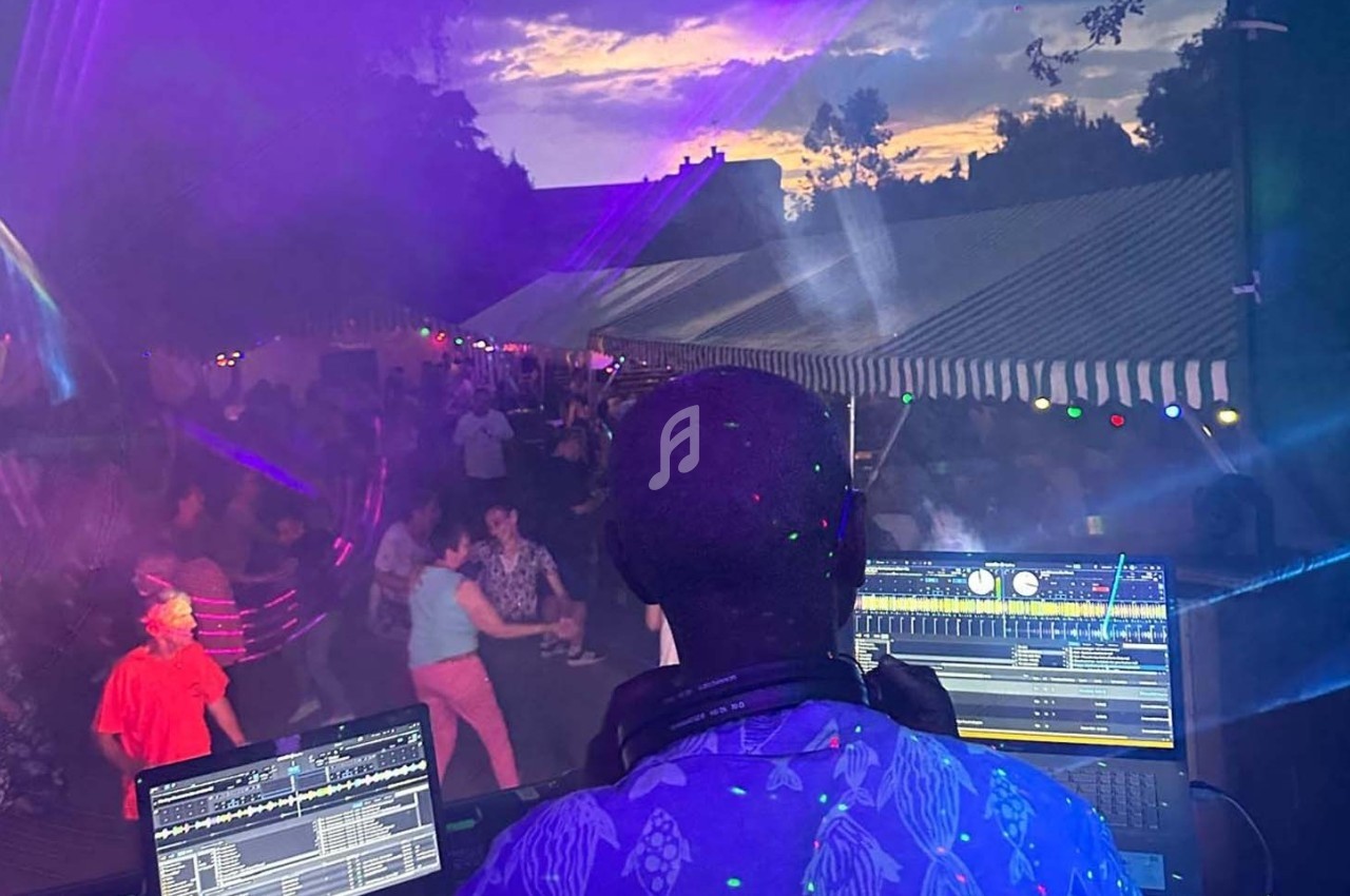 Un DJ mixe en plein air devant une foule dansante lors d'une soirée sous des tentes éclairées au crépuscule.