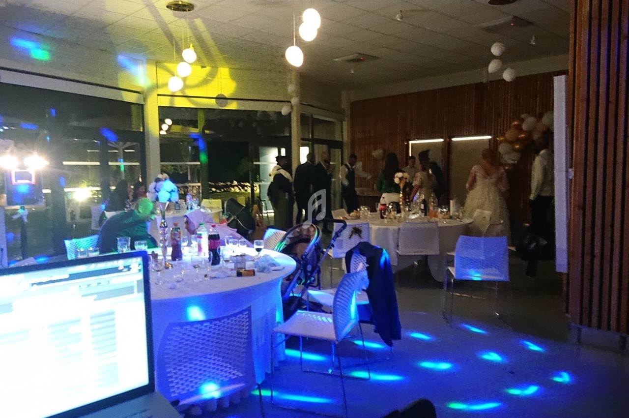 Salle de réception éclairée avec des invités debout et assis autour de tables décorées, ambiance festive avec jeux de…