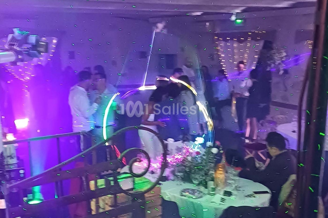 Des invités dansent sous des lumières colorées lors d'une fête, avec des tables décorées en arrière-plan.