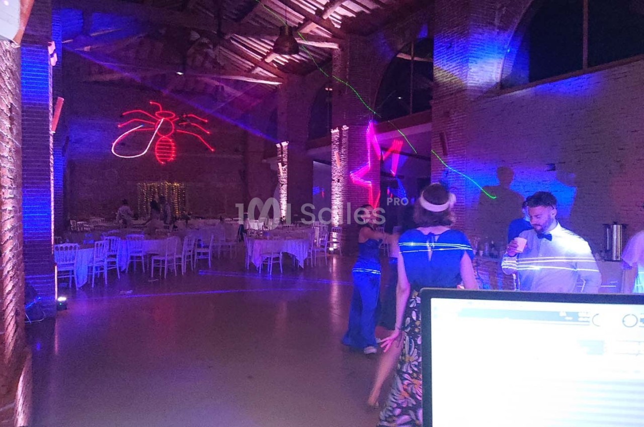 Salle de réception avec éclairages colorés, invités dansant et tables dressées en arrière-plan.