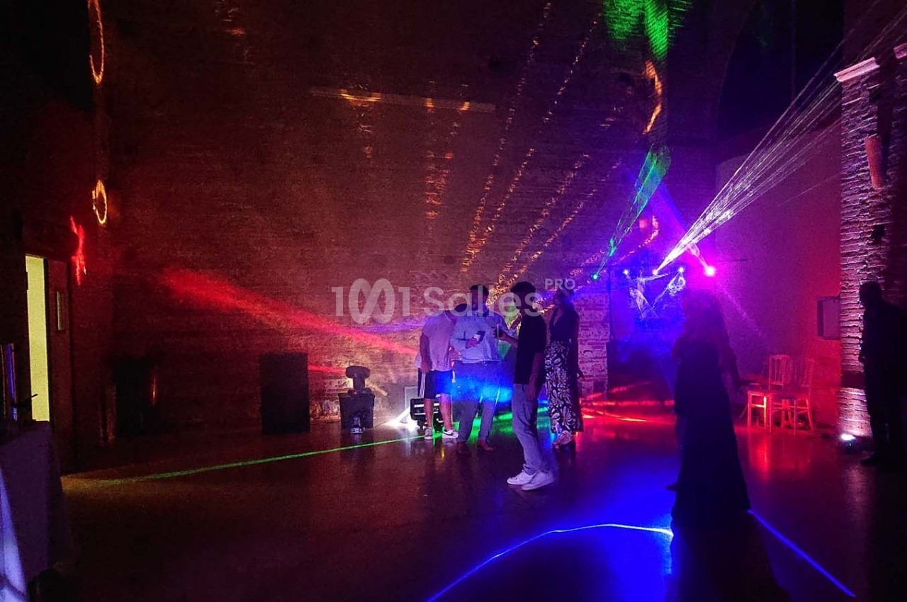 Des personnes discutent dans une salle sombre éclairée par des lumières colorées et des faisceaux laser.