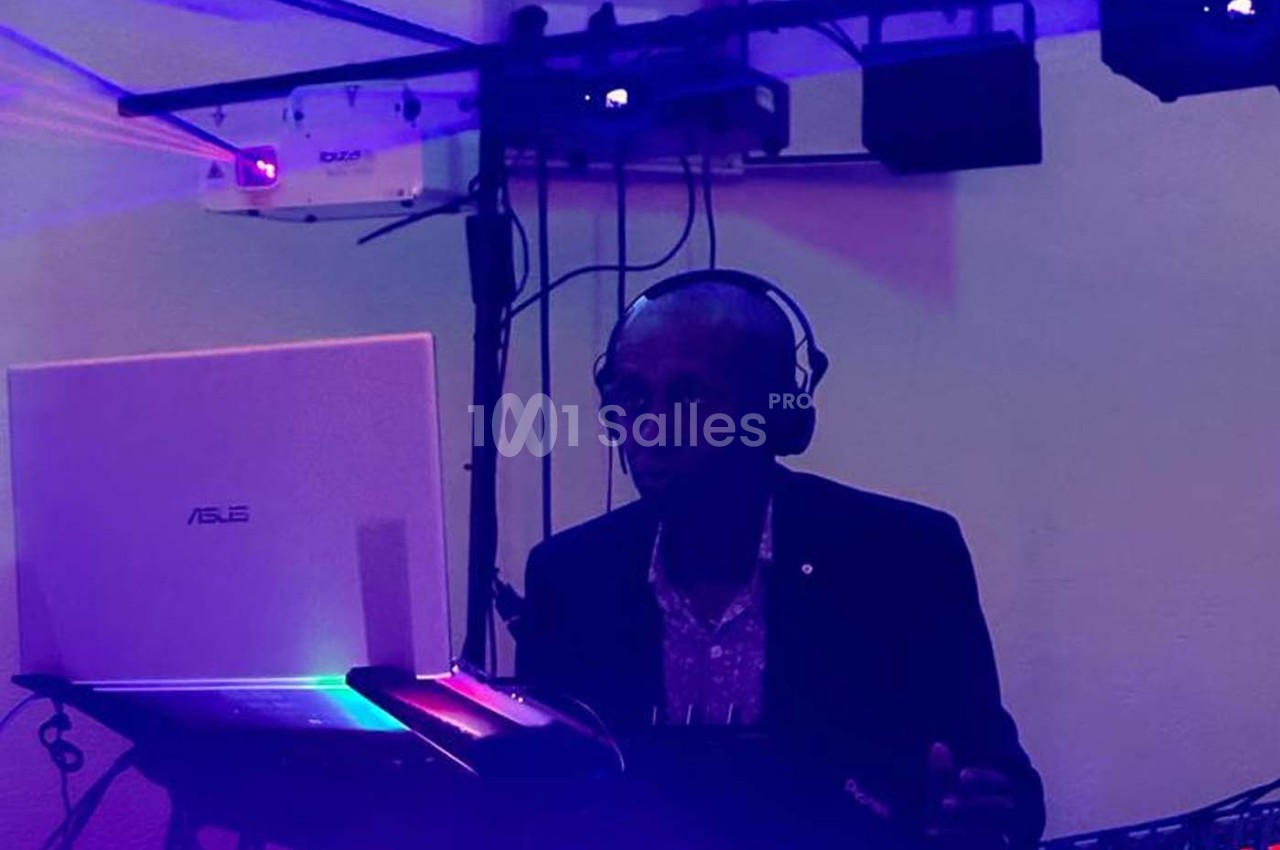 Un DJ portant un casque audio mixe de la musique sur un ordinateur portable dans une ambiance lumineuse tamisée.