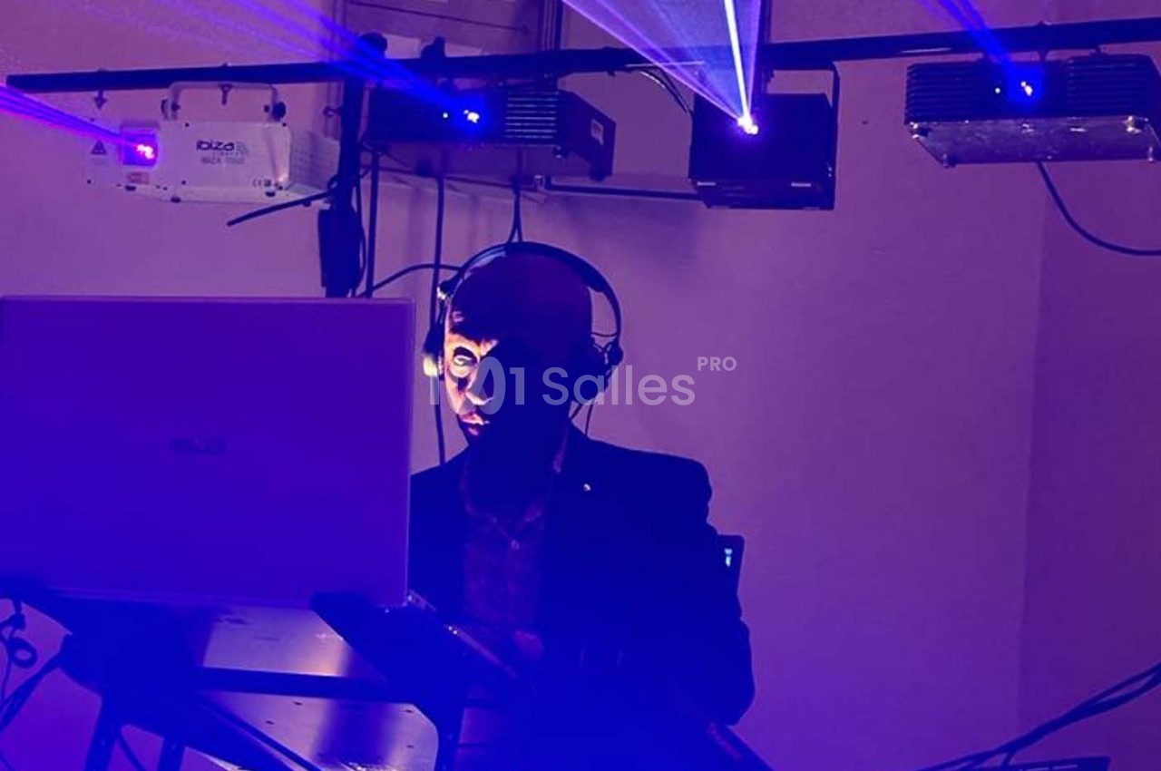Un DJ mixe de la musique dans une ambiance lumineuse avec des faisceaux laser bleus.