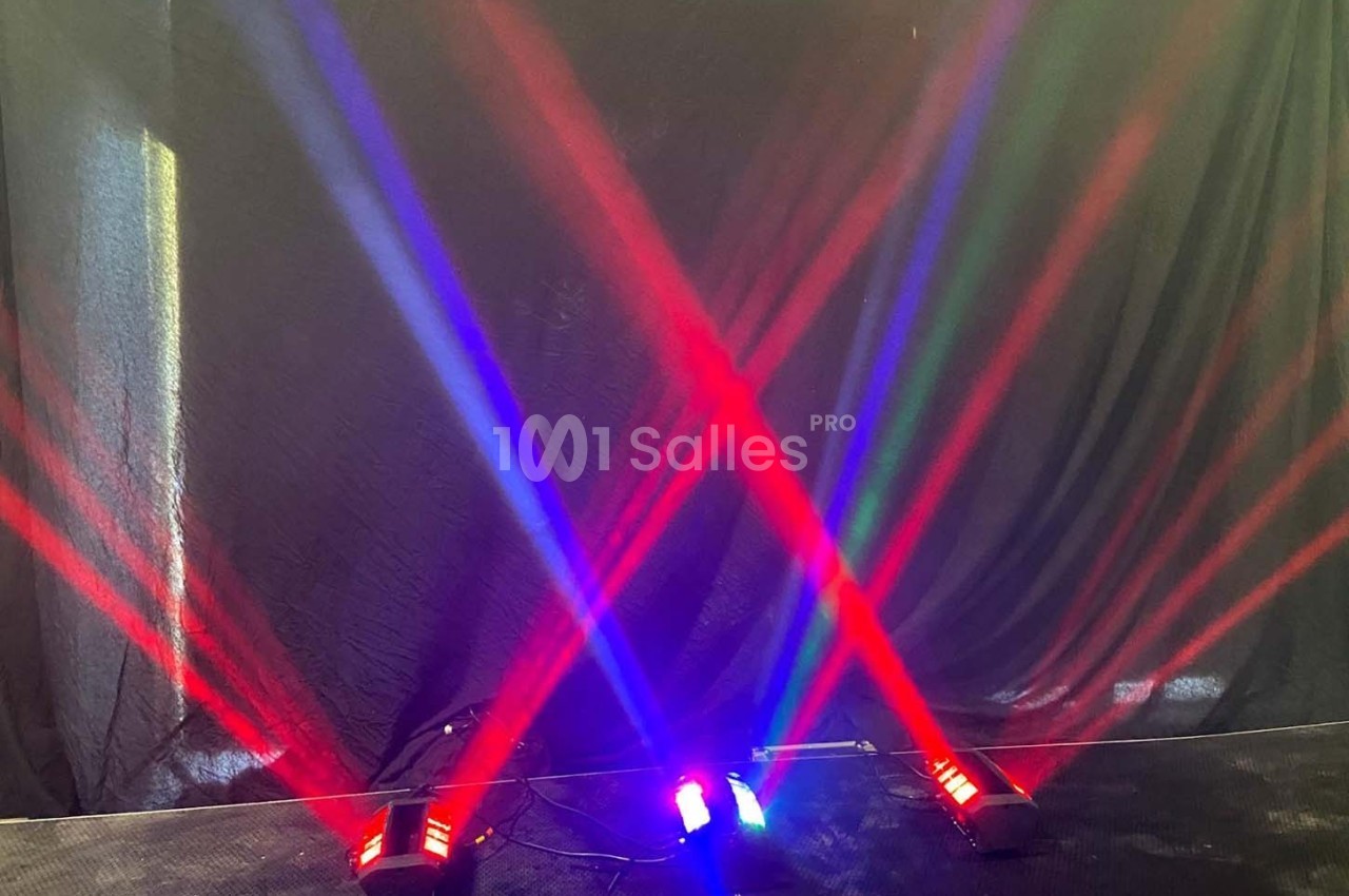 Faisceaux lumineux rouges, bleus et verts projetés en croix sur un fond noir dans un environnement sombre.