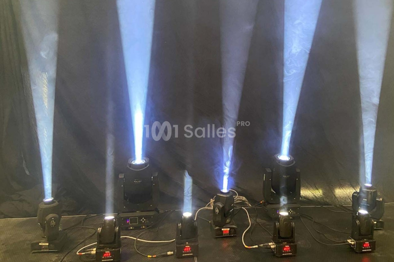 Projecteurs lumineux diffusant des faisceaux blancs sur un fond sombre, alignés sur une scène ou un espace intérieur.