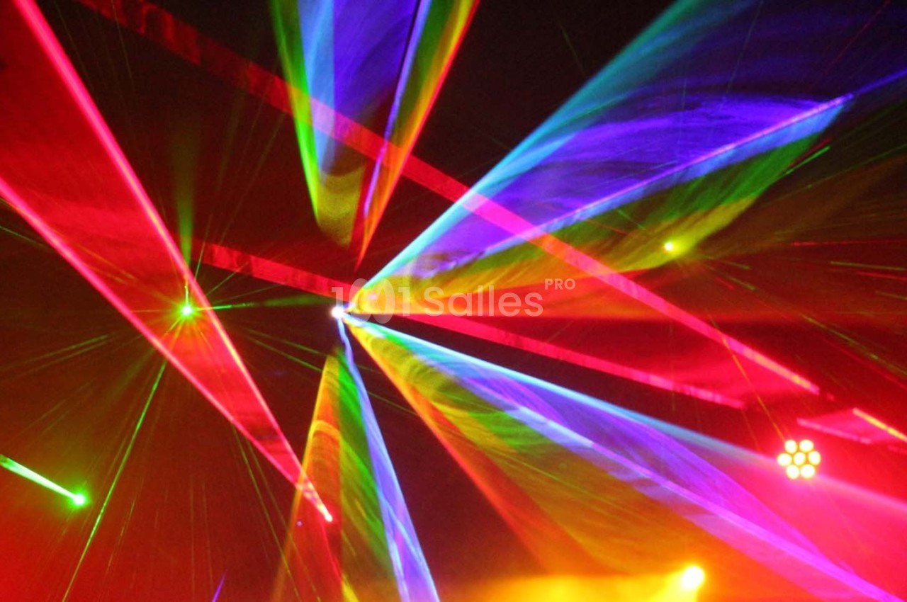Faisceaux lumineux multicolores traversant une scène sombre, créant un effet visuel dynamique.