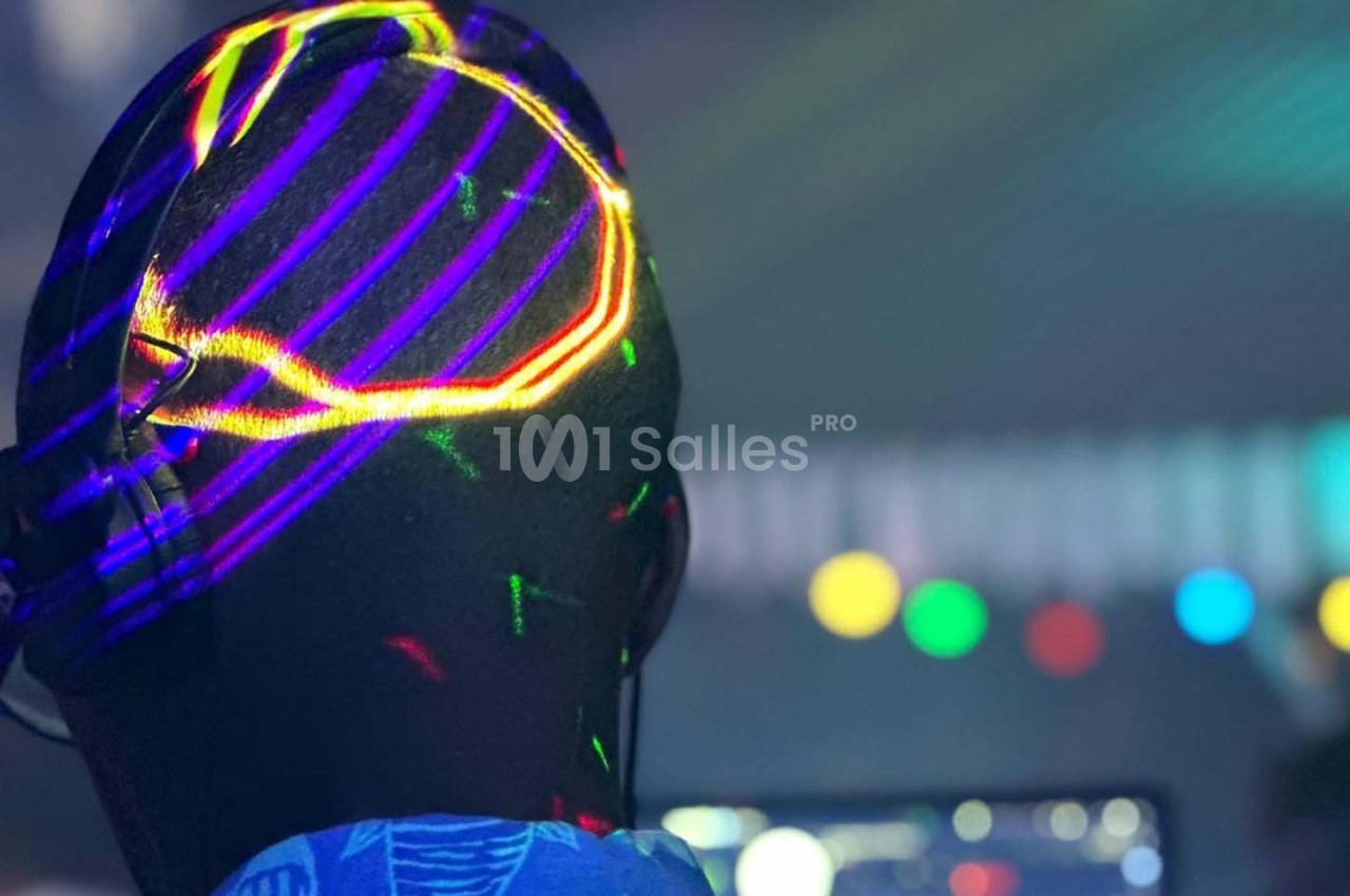 Une personne de dos portant un casque audio, éclairée par des lumières colorées dans un environnement sombre.