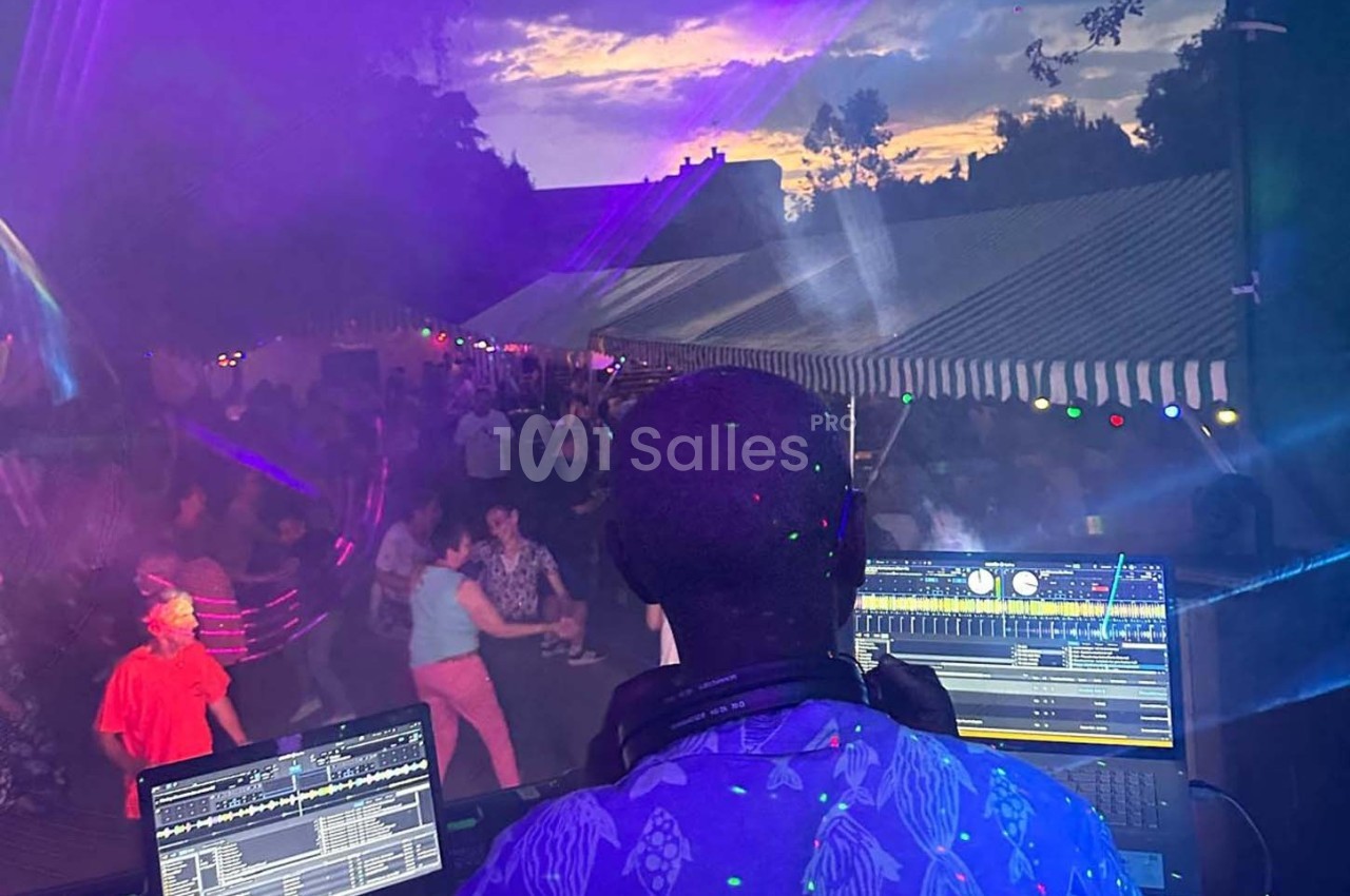Un DJ mixe en plein air devant une foule dansante sous des tentes éclairées au crépuscule.