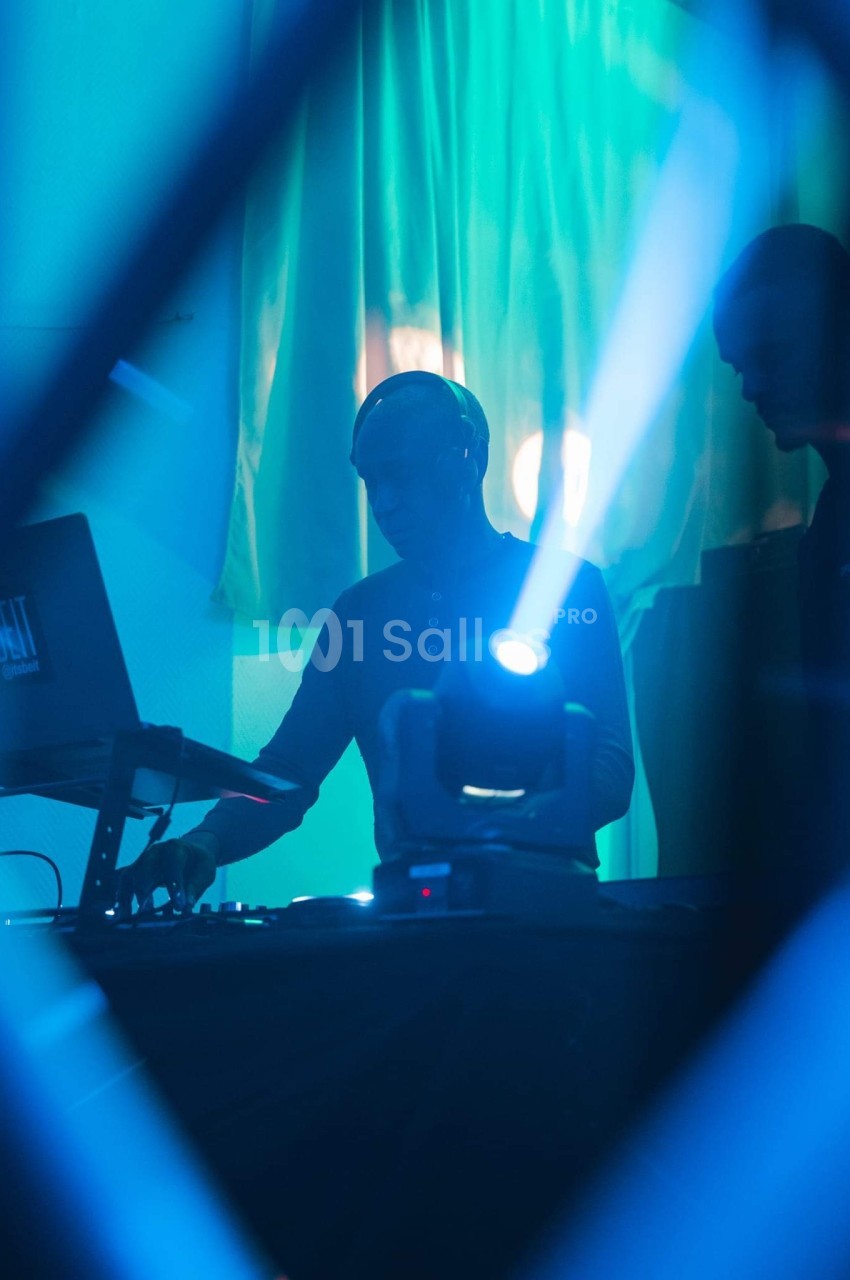 Un DJ mixant sur une scène éclairée par des lumières bleues, avec un projecteur lumineux au premier plan.
