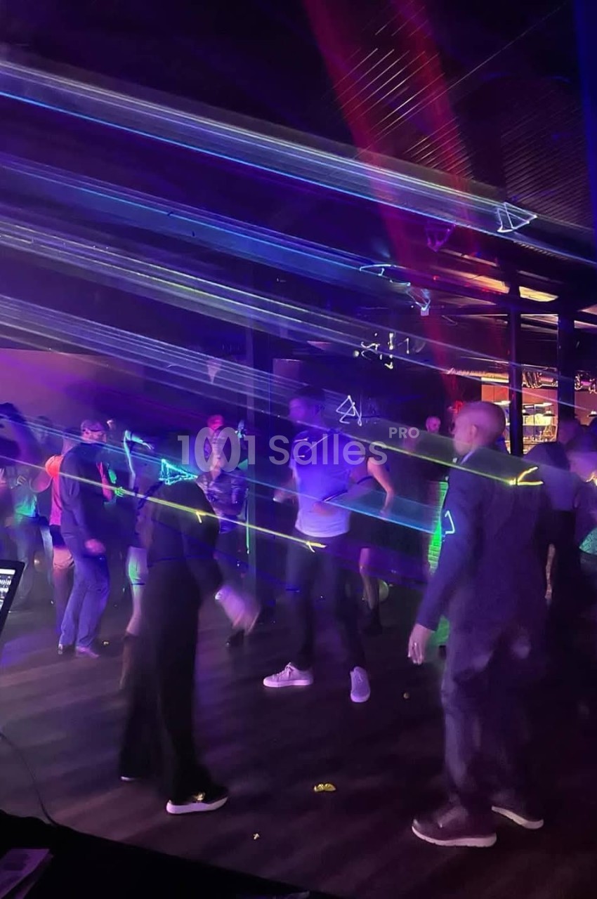 Personnes dansant dans une ambiance sombre avec des lumières laser colorées traversant la salle.