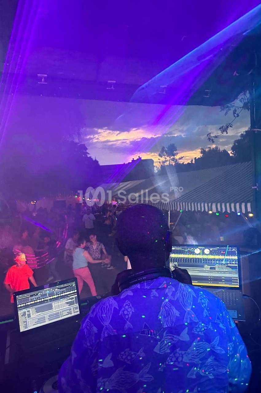 Un DJ mixant en plein air au coucher du soleil, avec une foule dansante et des jeux de lumière colorés.