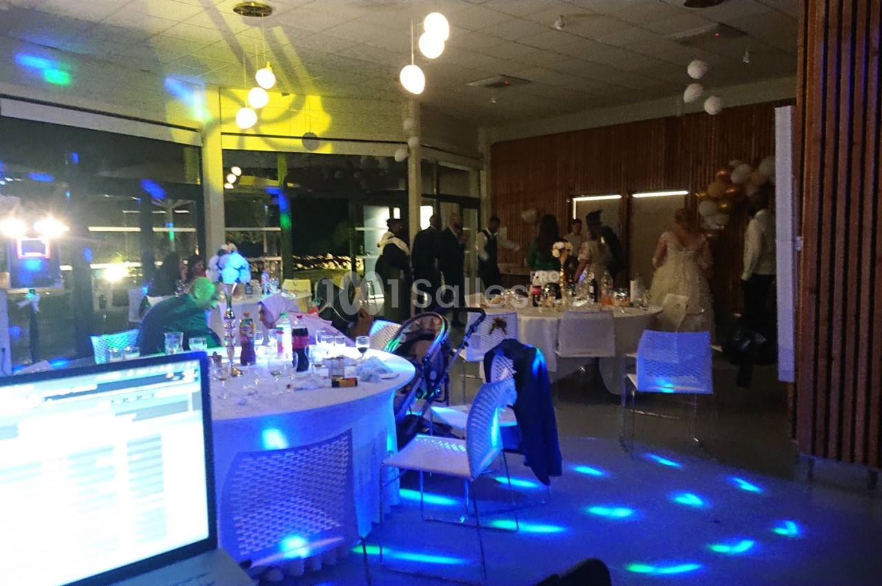 Salle de réception illuminée avec des invités, tables dressées et ambiance festive en soirée.
