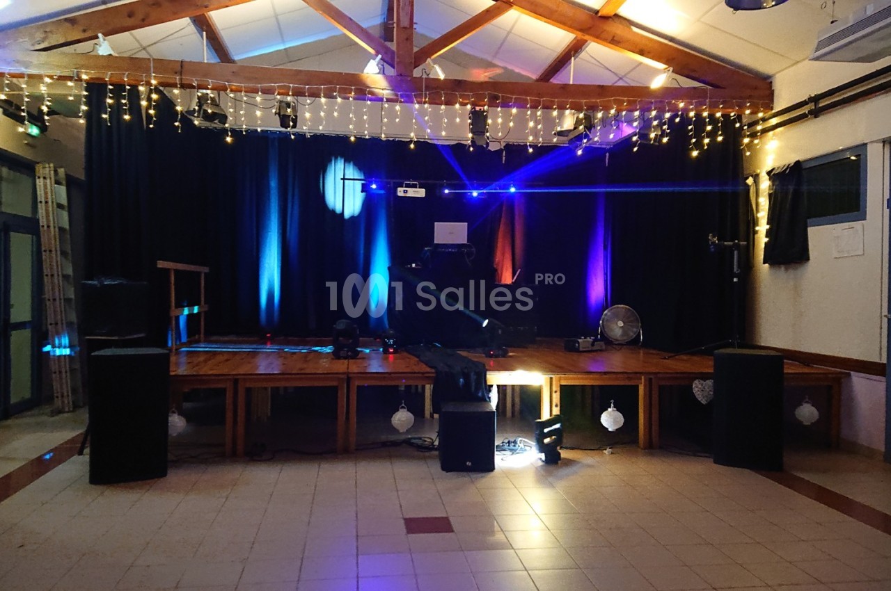 Scène décorée avec guirlandes lumineuses, éclairages colorés et équipements audio dans une salle intérieure.