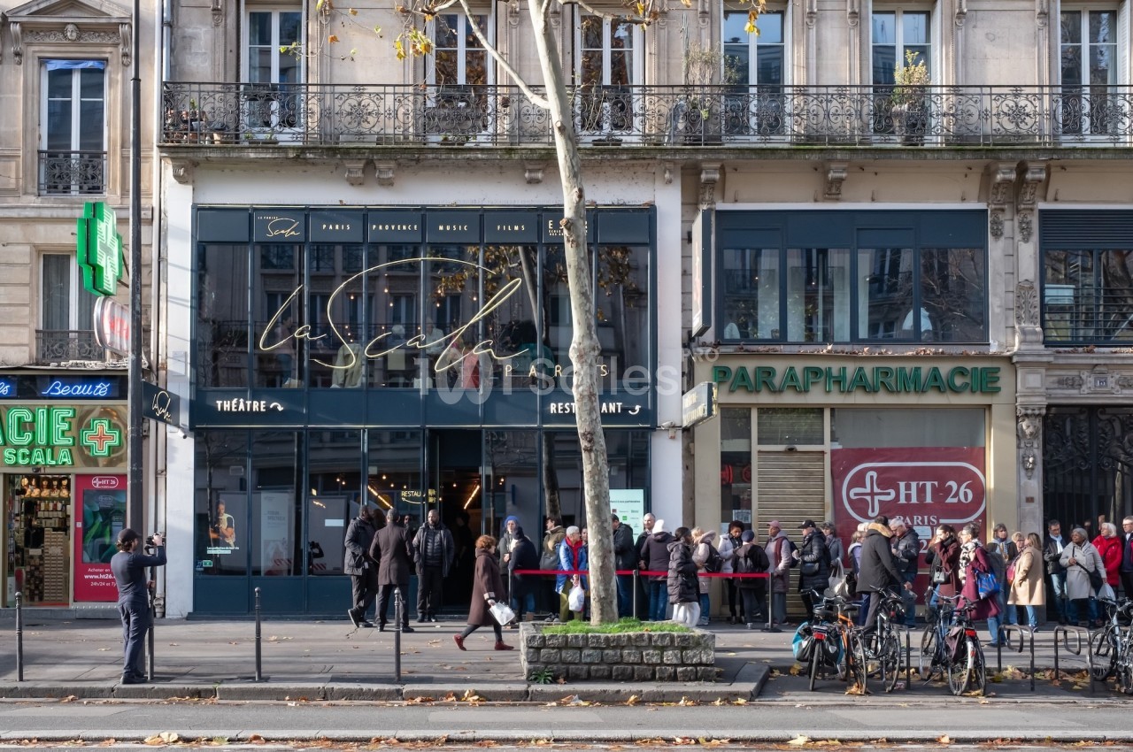 Façade d'un théâtre et d'une parapharmacie sur une avenue parisienne, avec des passants et des vélos stationnés.