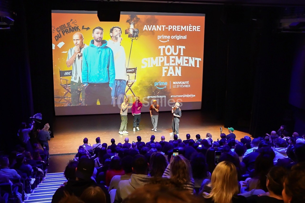 Quatre personnes sur scène devant un public, lors d'une avant-première avec une affiche projetée en arrière-plan.