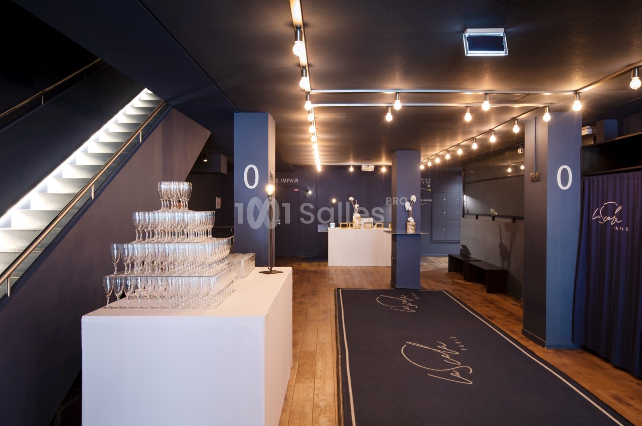 Hall d'entrée élégant avec moquette bleue, comptoir d'accueil, présentoir de coupes et éclairage chaleureux.