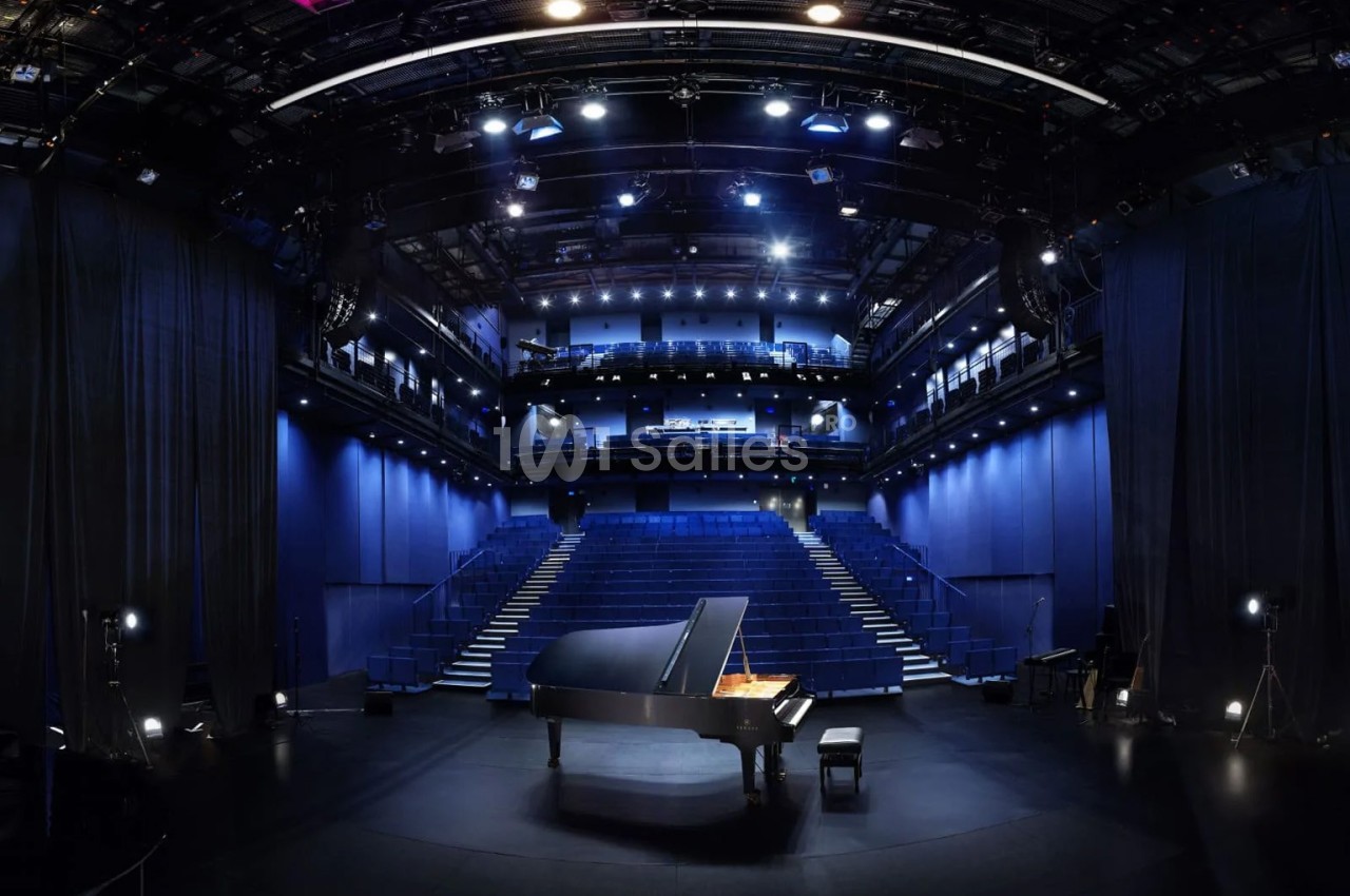 Salle de spectacle vide avec un piano à queue noir au centre de la scène, éclairée par des projecteurs.
