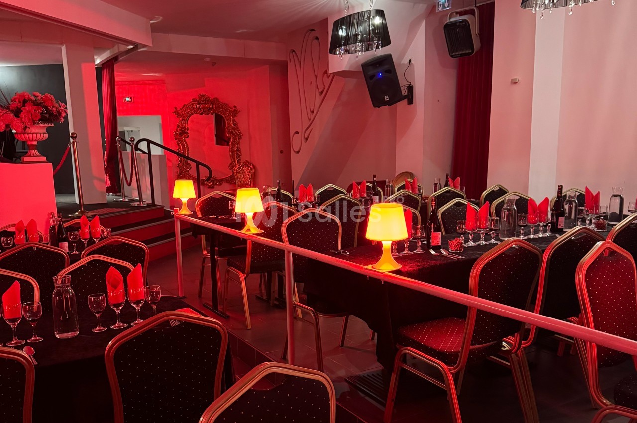 Salle de réception avec tables dressées, nappes noires, serviettes rouges et lampes d'ambiance diffusant une lumière chaude.