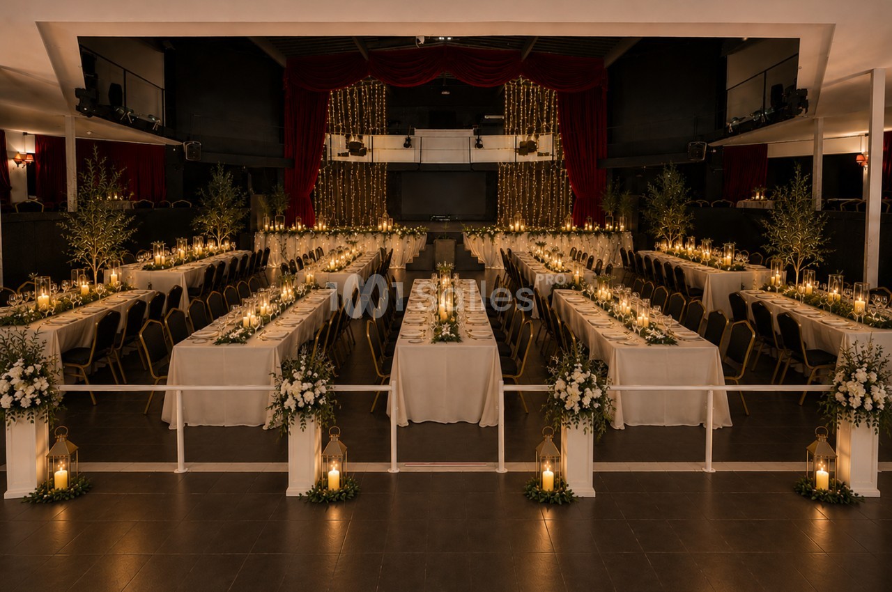 Salle de réception décorée avec des tables alignées, bougies, guirlandes lumineuses et arrangements floraux élégants.