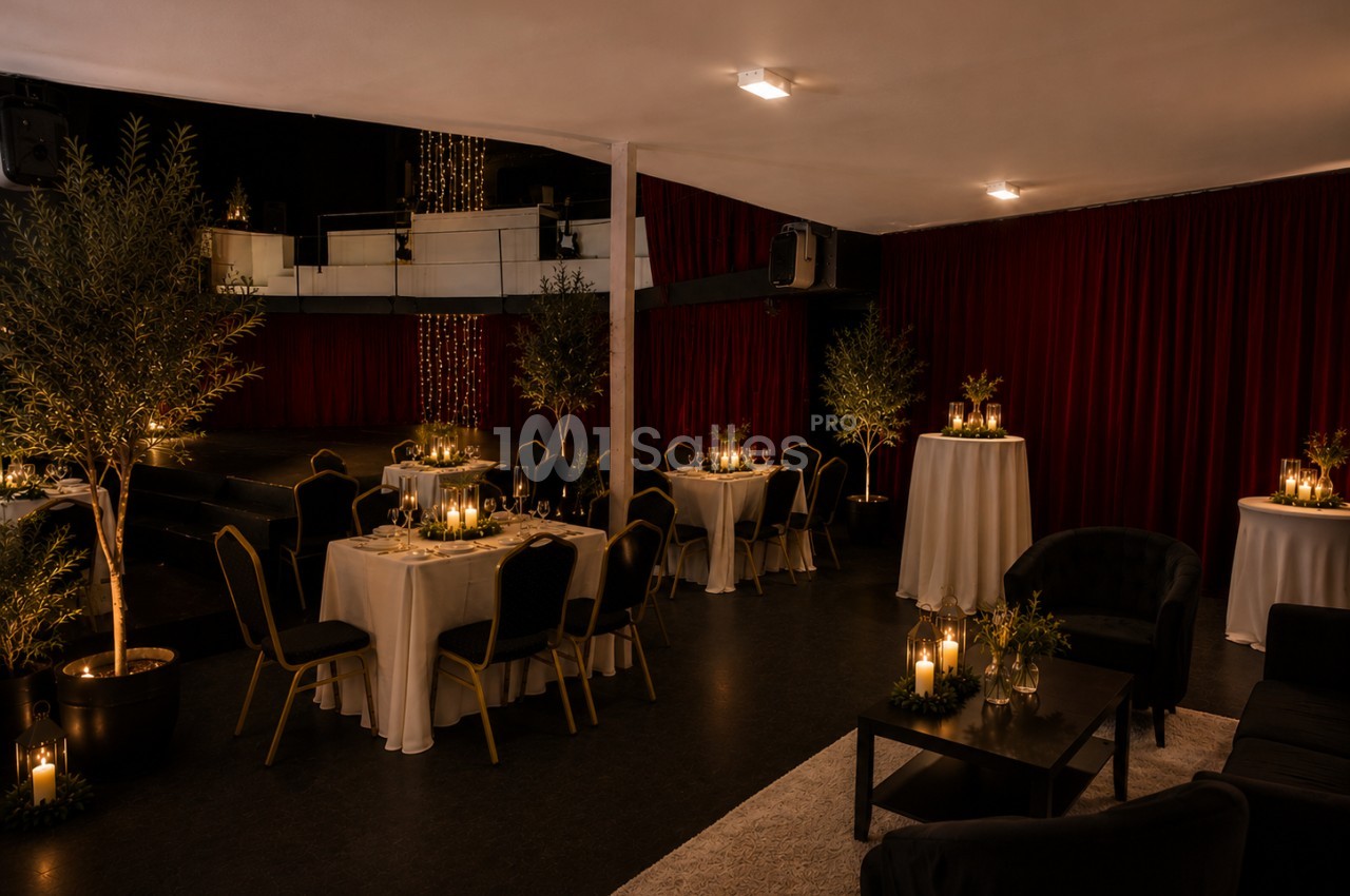 Salle décorée pour un événement, avec tables dressées, bougies, plantes et rideaux rouges en arrière-plan.