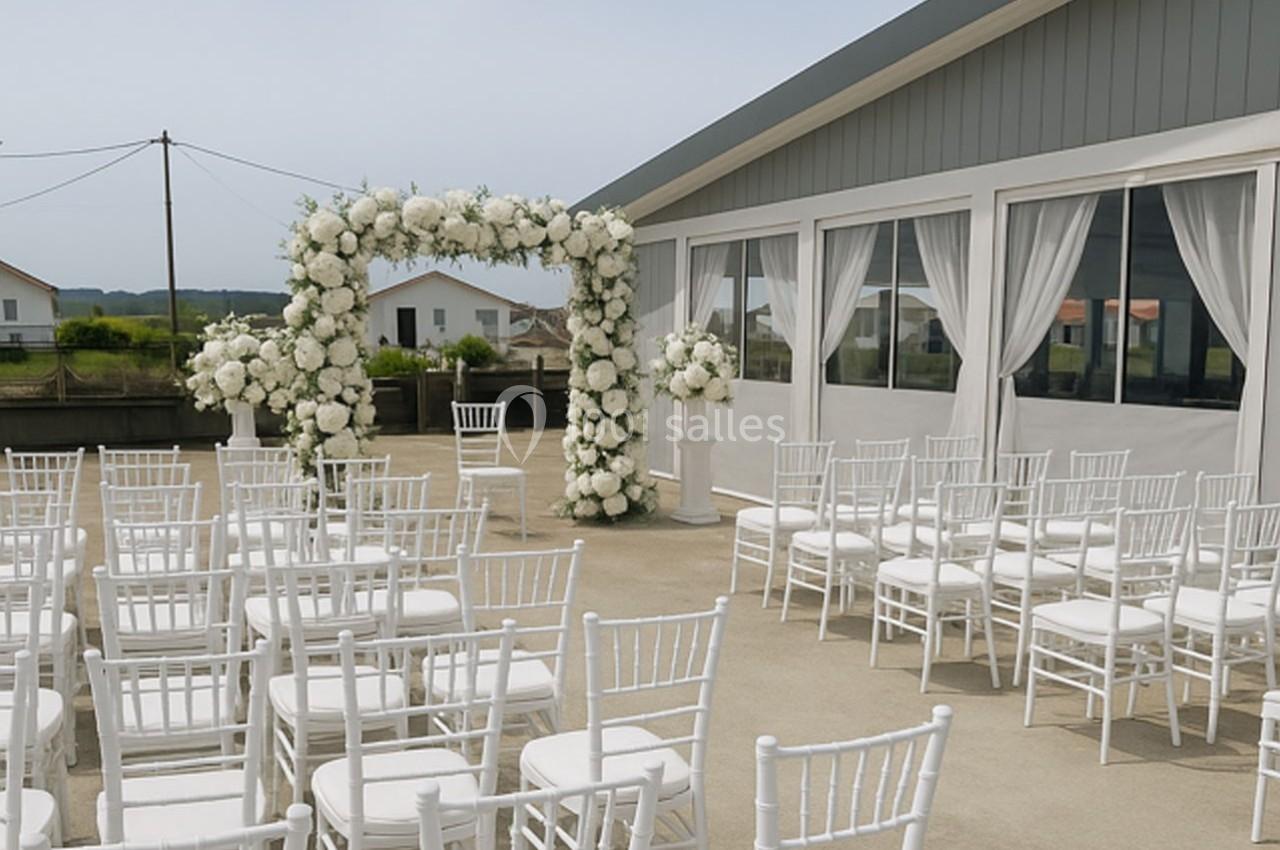Chaises blanches alignées devant une arche florale blanche dans un espace extérieur près d'un bâtiment moderne.