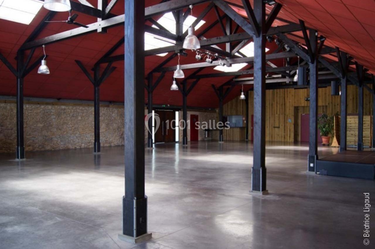 Salle spacieuse avec charpente apparente en bois, murs en pierre et sol en béton poli, éclairée par des fenêtres en toiture.