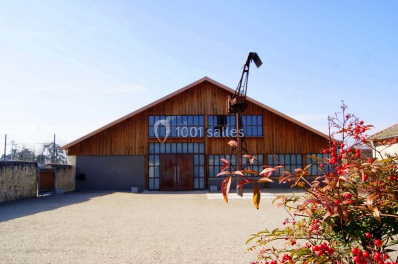 Bâtiment en bois avec de grandes baies vitrées, situé dans une cour gravillonnée sous un ciel dégagé.