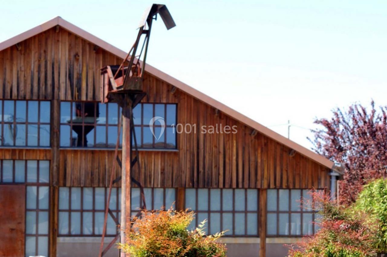Bâtiment en bois avec de grandes fenêtres, entouré de végétation, et une structure métallique élancée au premier plan.