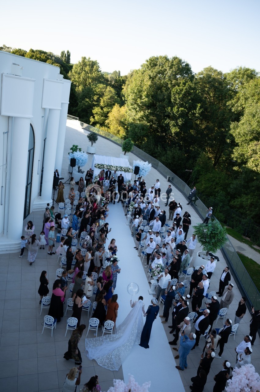 Cérémonie de mariage en extérieur avec des invités assis le long d'une allée blanche, entourée de verdure.
