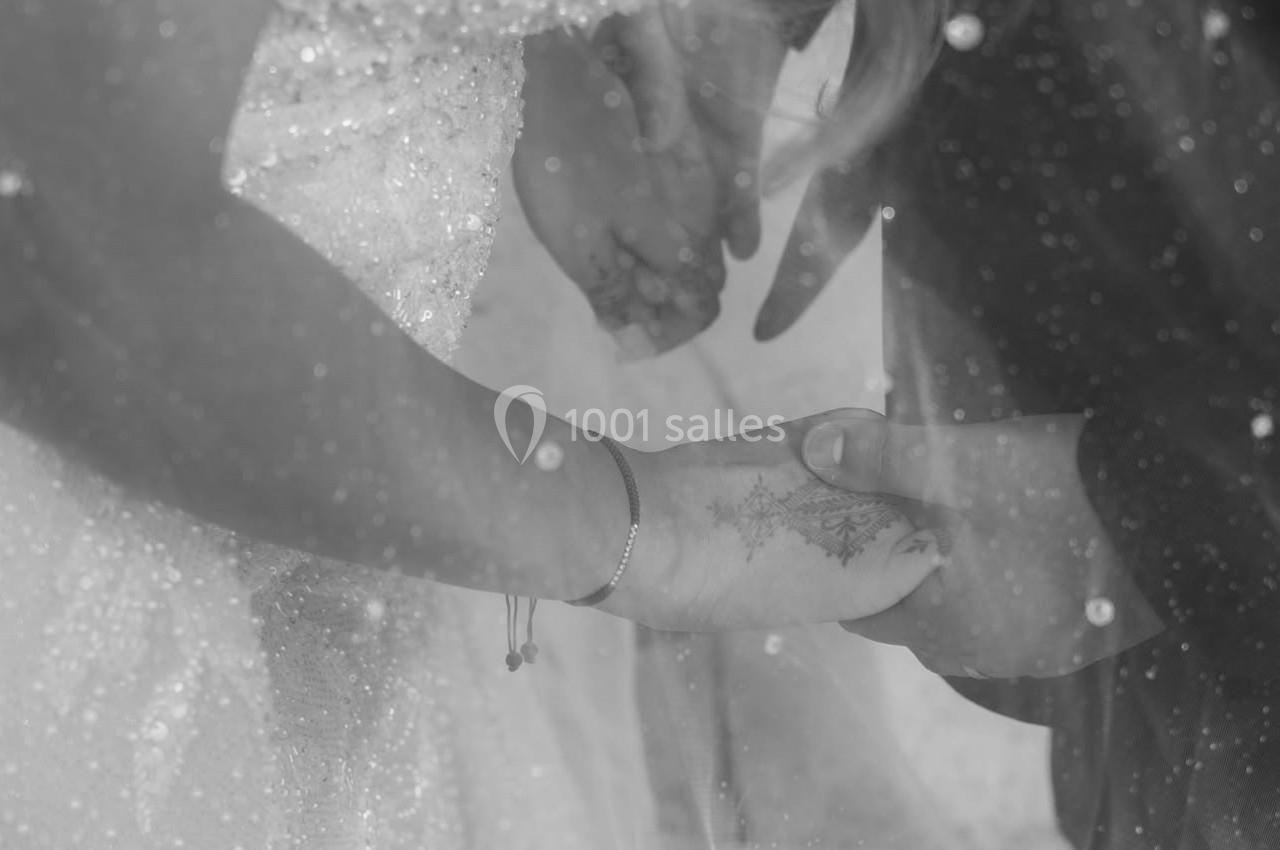 Deux personnes se tenant les mains, vêtues de tenues de mariage, avec un voile transparent en premier plan.