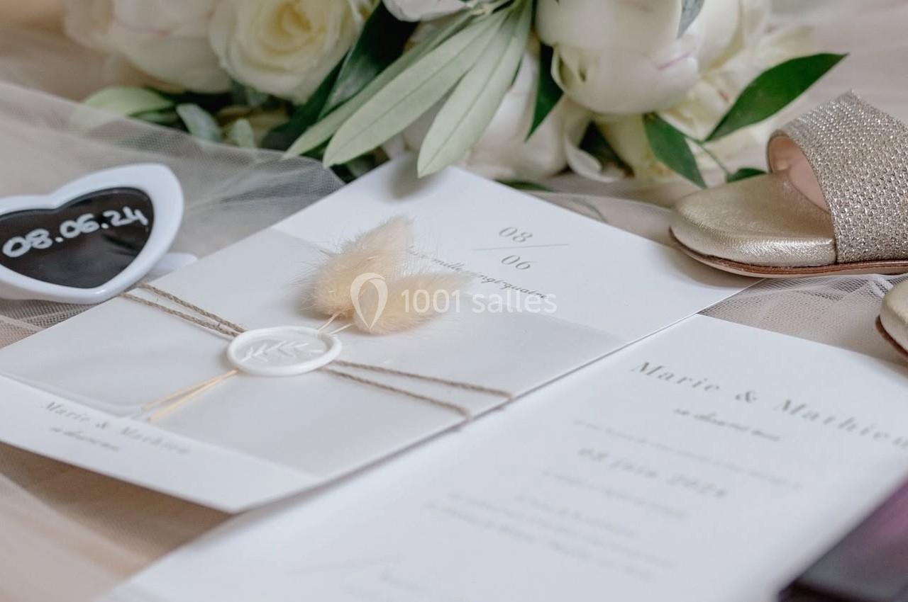 Bouquet de roses blanches, faire-part de mariage, sandales dorées et accessoires disposés sur un voile beige.