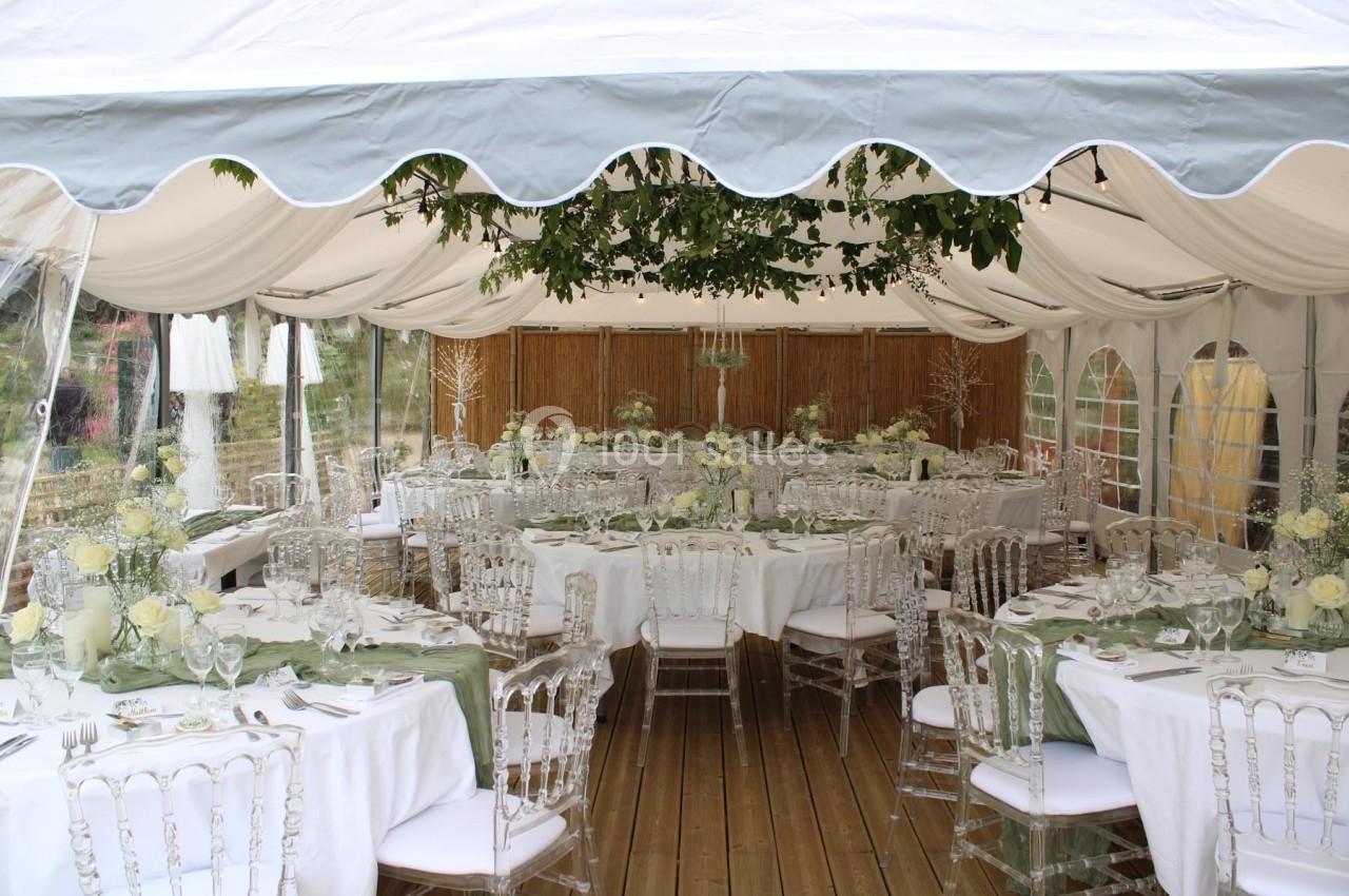 Salle de réception sous une tente blanche, décorée avec des tables rondes, nappes vertes et chaises transparentes.