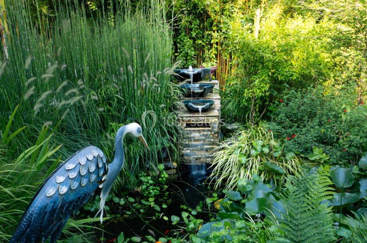 Jardin verdoyant avec une fontaine en pierre, un bassin rempli de plantes aquatiques et une sculpture d'oiseau.