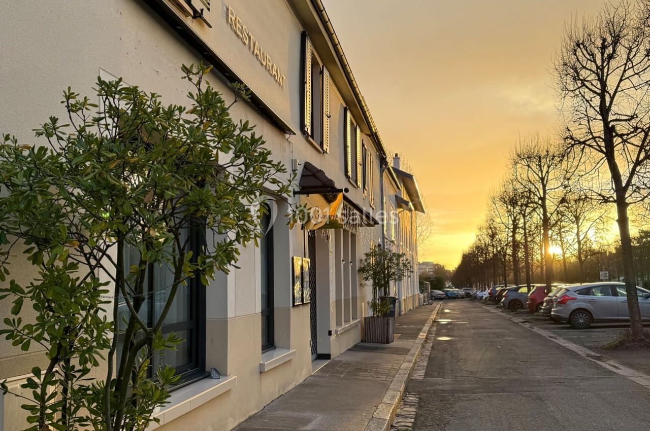 Façade d'un restaurant et d'immeubles au coucher du soleil, avec une rue bordée d'arbres et de voitures.
