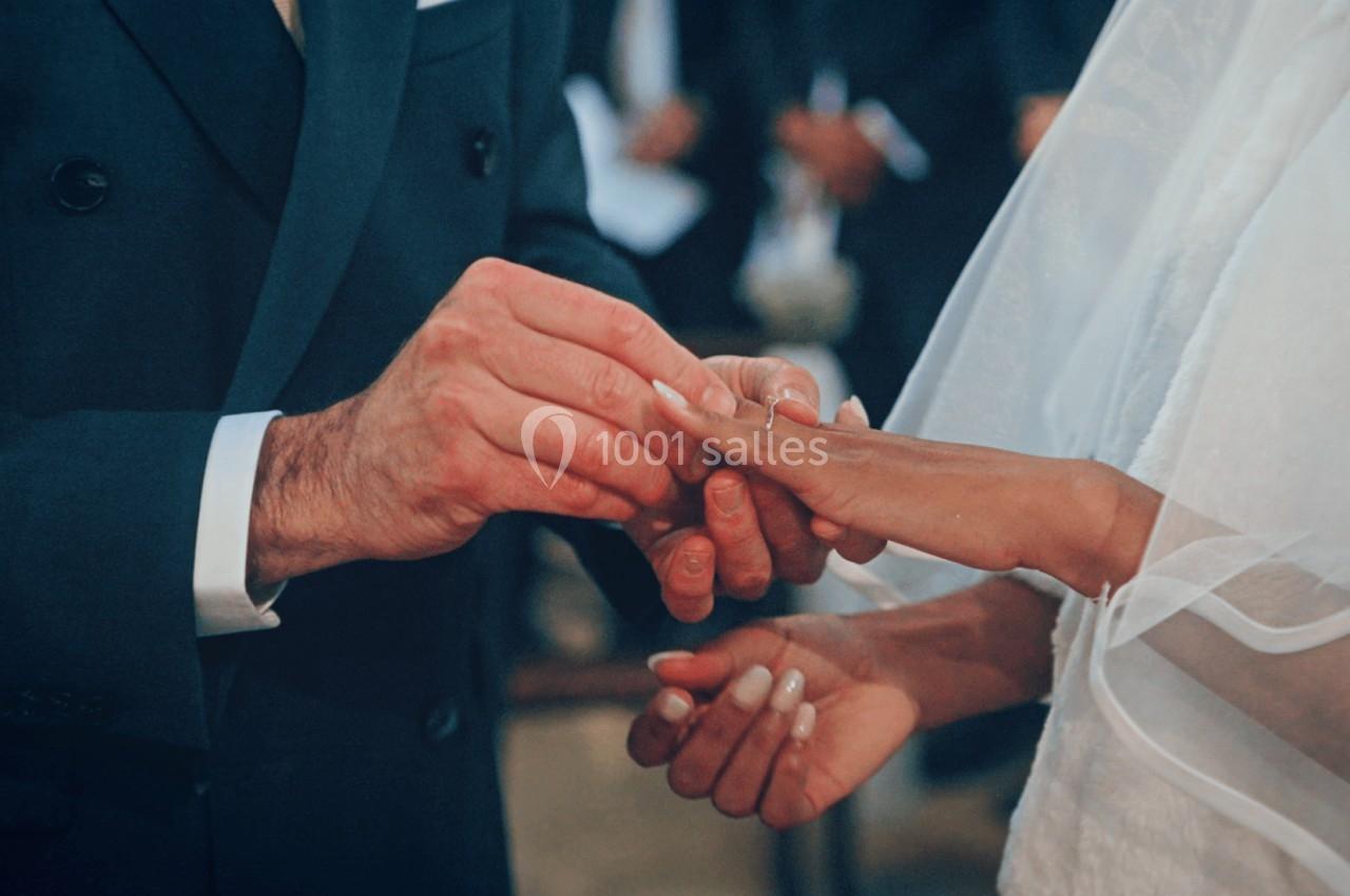 Un homme passe une alliance au doigt d'une femme vêtue d'une robe blanche lors d'une cérémonie.