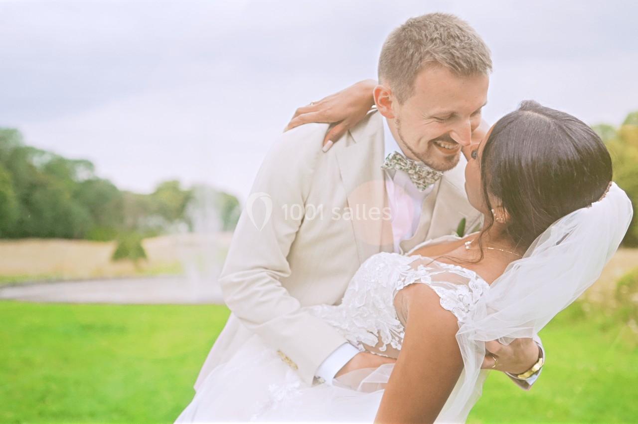 Un couple de mariés s'enlace dans un parc verdoyant sous une lumière douce.