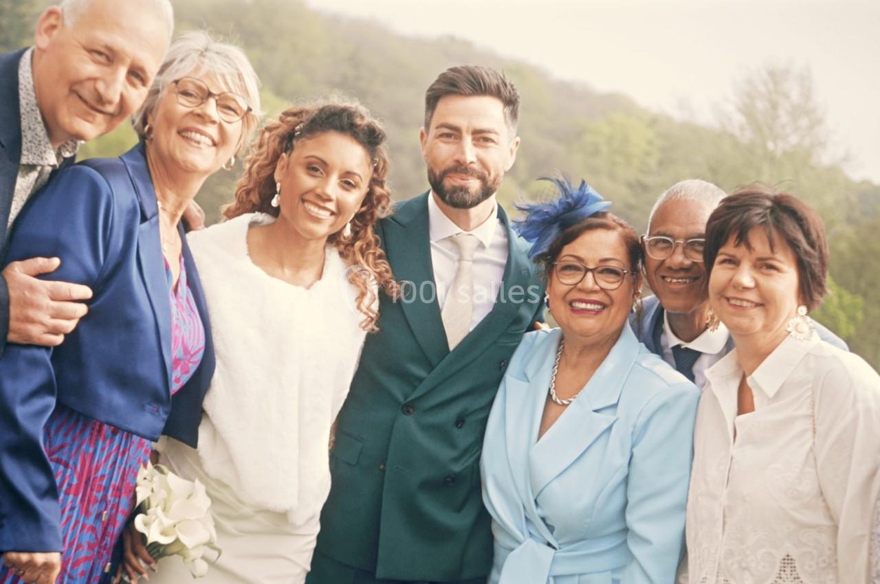 Un groupe de personnes souriantes pose ensemble à l'extérieur, avec un couple au centre en tenue de mariage.