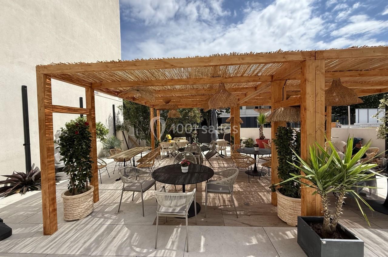 Terrasse aménagée avec pergola en bois, mobilier d'extérieur, plantes en pots et ciel partiellement nuageux.