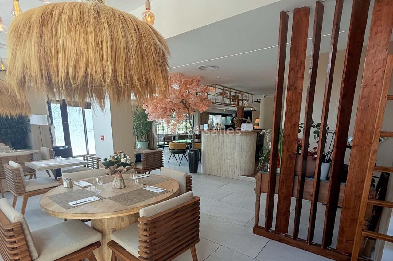 Salle de restaurant lumineuse avec décoration naturelle, tables en bois, chaises rembourrées et luminaires en fibres…