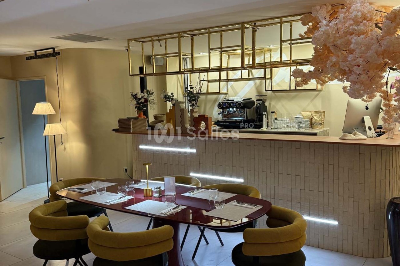 Salle de restaurant élégante avec table dressée, chaises vertes, bar en arrière-plan et décoration florale.