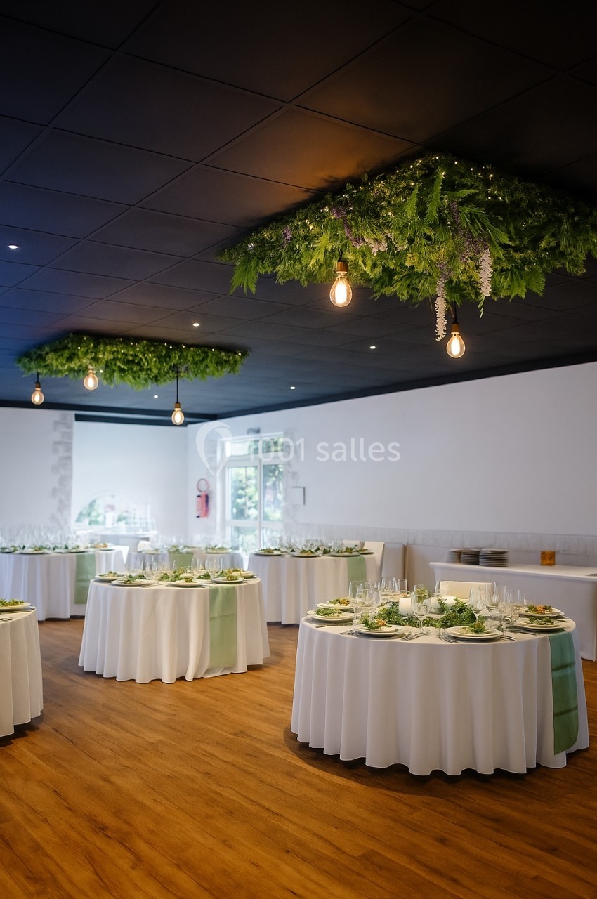 Salle de réception décorée, tables rondes dressées avec nappes blanches et centres de table végétaux, plafond orné de…