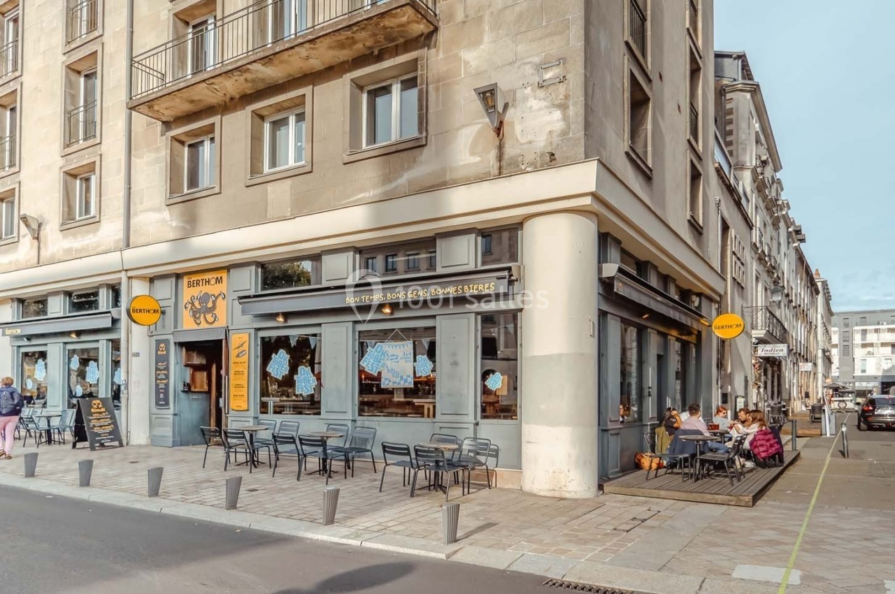 Façade d'un restaurant d'angle avec terrasse extérieure, tables occupées et enseignes visibles sur une rue urbaine.